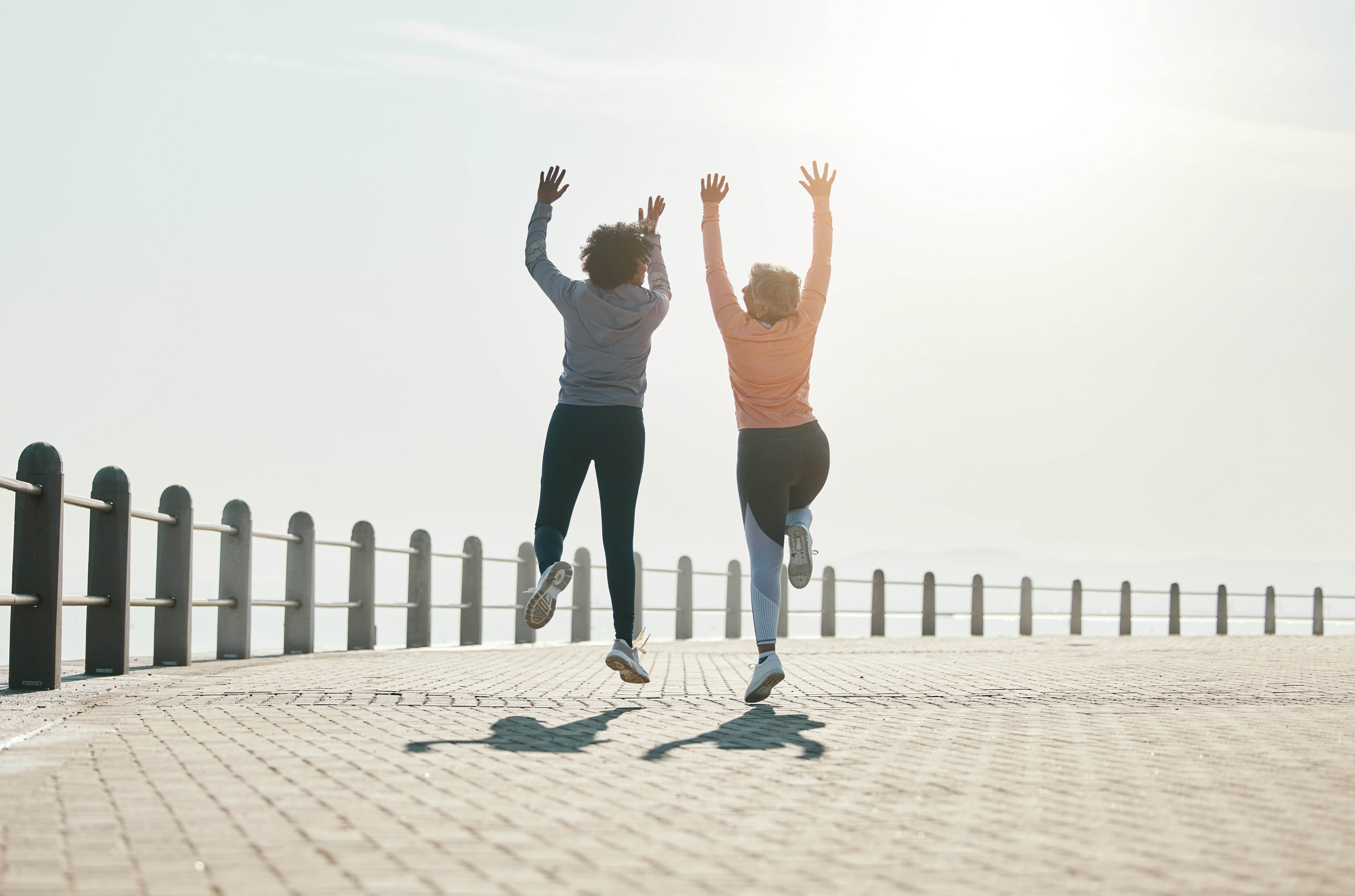 Two women jump off the ground in celebration, next to a fence around the water's edge Two women jump off the ground in celebration, next to a fence around the water's edge